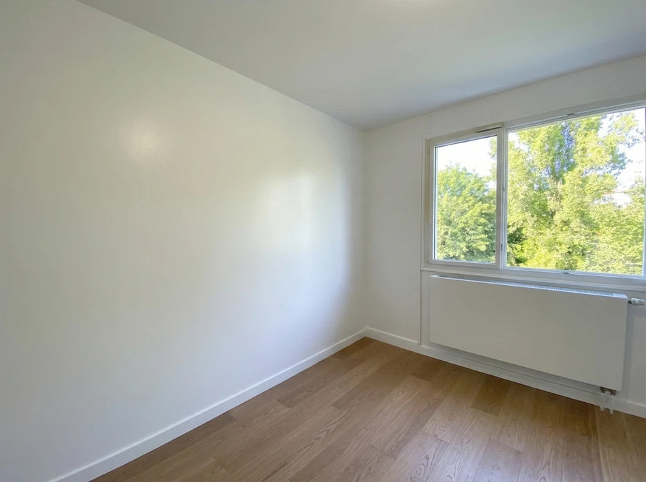 Pièce vide, lumineuse, murs blancs, parquet stratifié chêne clair