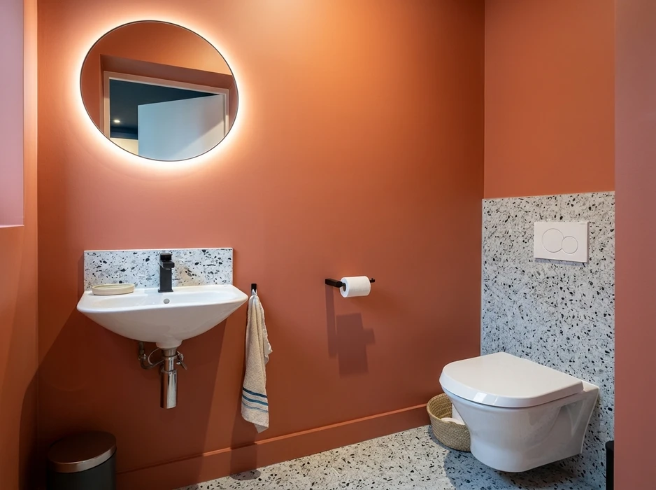 Salle de bain design aux murs terracotta, carrelage terrazzo blanc moucheté noir en demi-hauteur