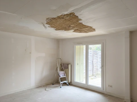 Intérieur, personne appliquant du papier peint beige texturé sur un mur, portant des gants de protection blancs en coton