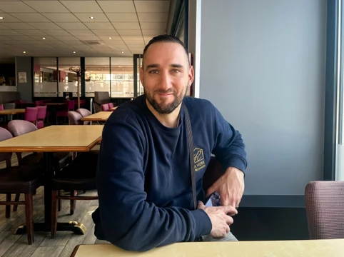 Intérieur d'appartement en cours de rénovation avec zone habitable terminée aux parquets clairs et murs blancs, contrastant avec espace de travail sous escalier
